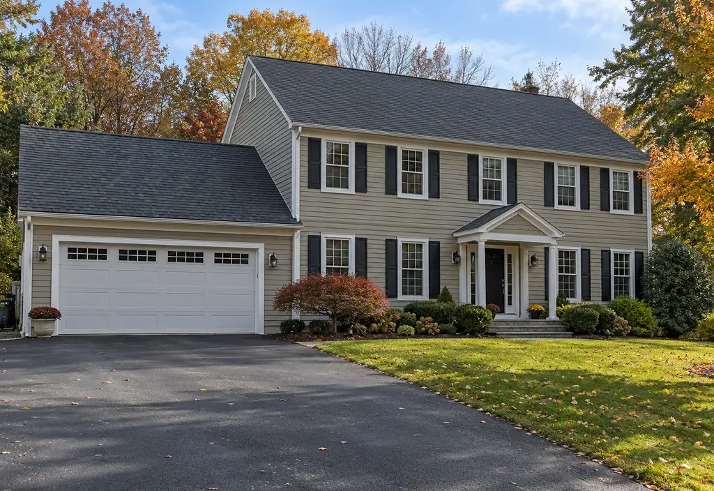 A two-story suburban house in the northeast with a new roof, photographed from the driveway on a calm day, a few leaves on the lawn