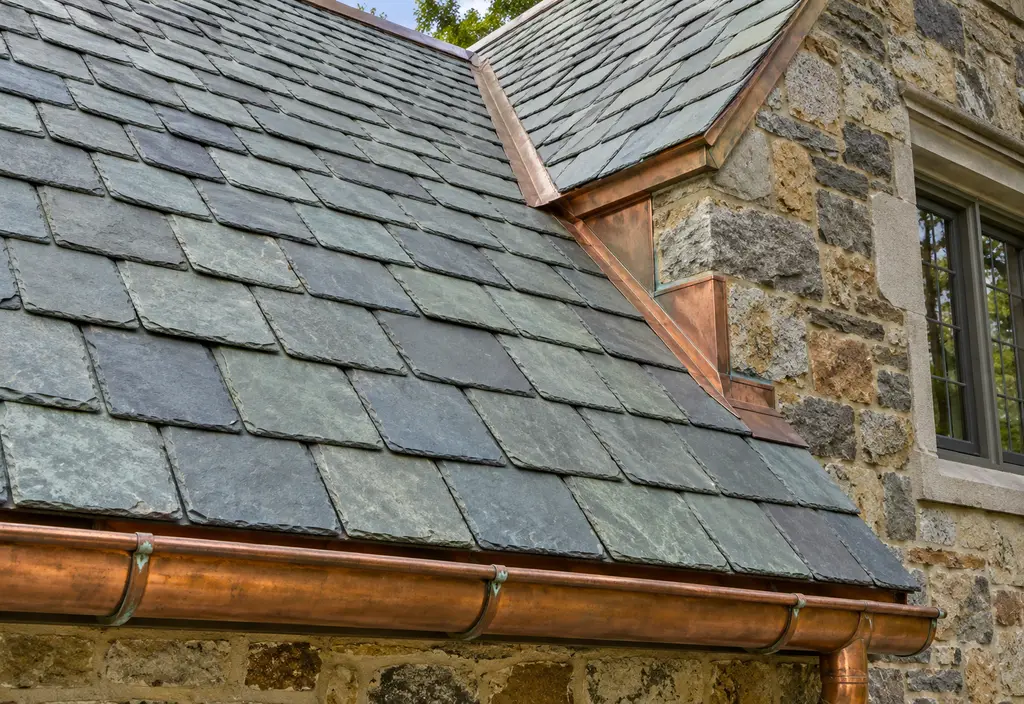 A historic stone house with a gray-green slate roof with copper flashing and a copper gutter, close view of the slate pattern